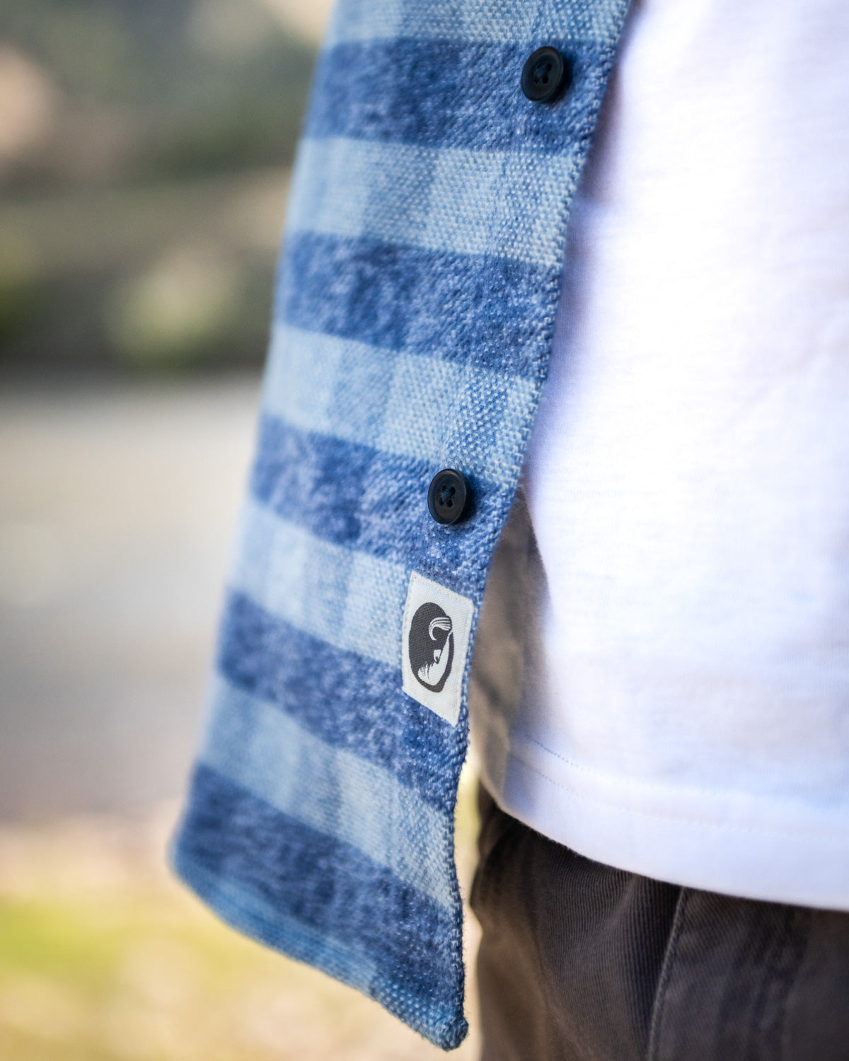 Blue checkered shirt with a brand logo worn by a person outdoors