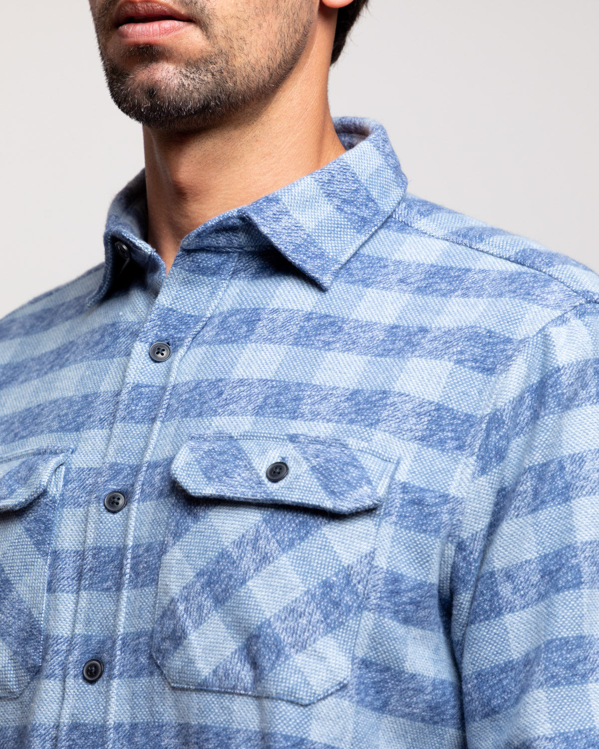 Close-up of a person wearing a blue plaid shirt against a neutral background