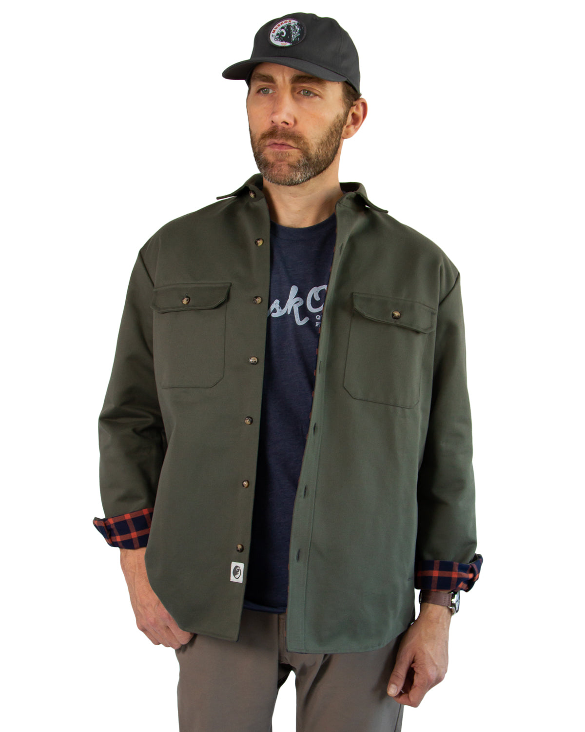 Man wearing a green jacket, navy t-shirt, and cap on a white background