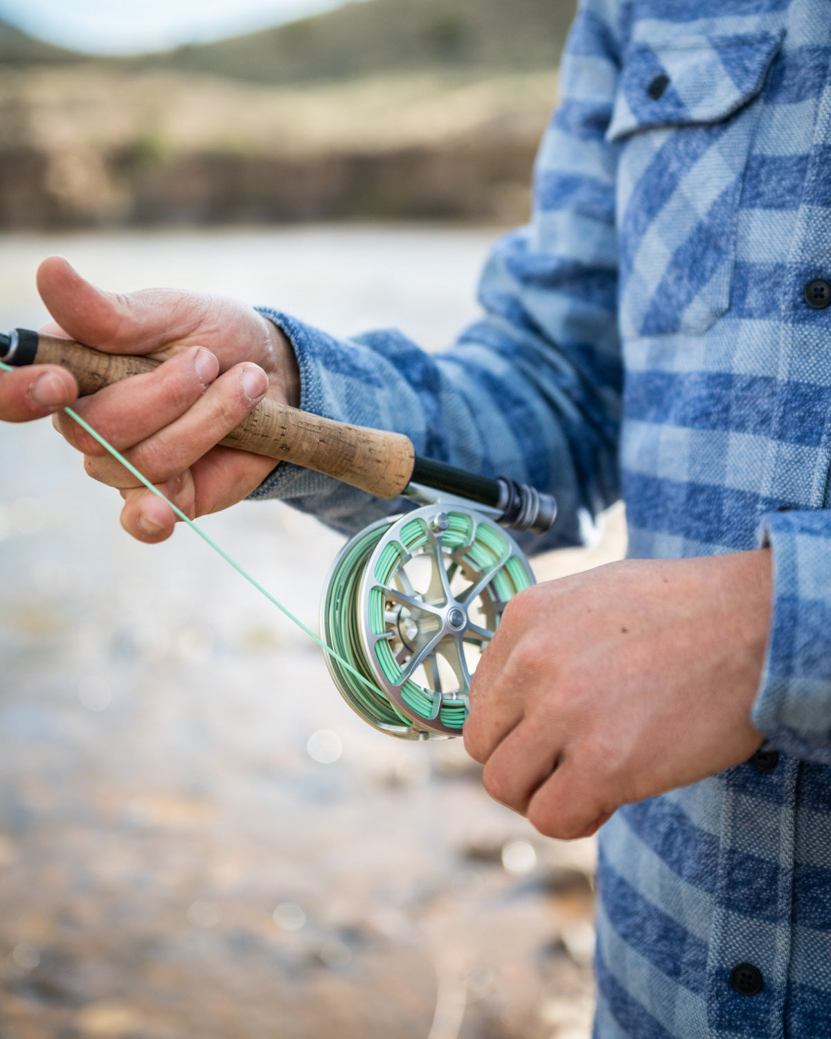 Person holding a fly fishing rod and reel by a body of water