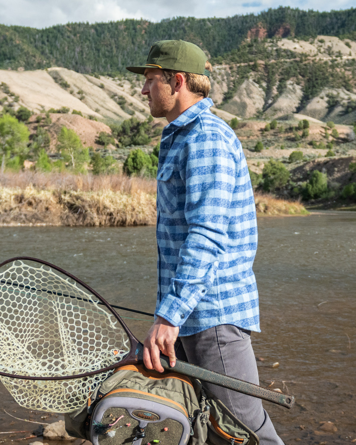 Man holding a fishing net by a river with mountains in the background